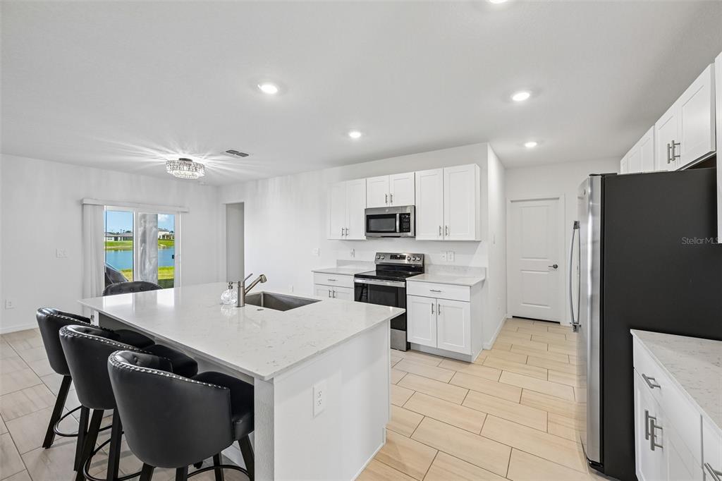 A modern kitchen features white cabinets, a quartz-topped island, stainless appliances, and tile flooring — 8807 SUNSET PARK TRAIL, PARRISH, FL