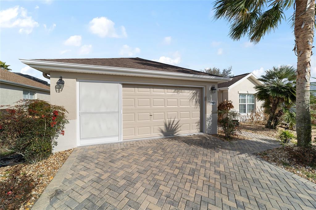 A beige house exterior features a two-car garage, a screen door, and a paved driveway — 12747 SE 97TH TERRACE ROAD, SUMMERFIELD, FL