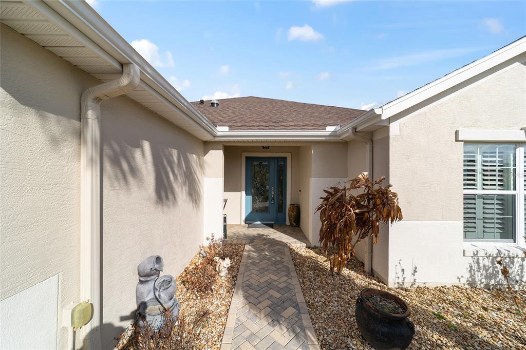 A paved walkway leads to the blue front door of a beige house with gravel landscaping — 12747 SE 97TH TERRACE ROAD, SUMMERFIELD, FL