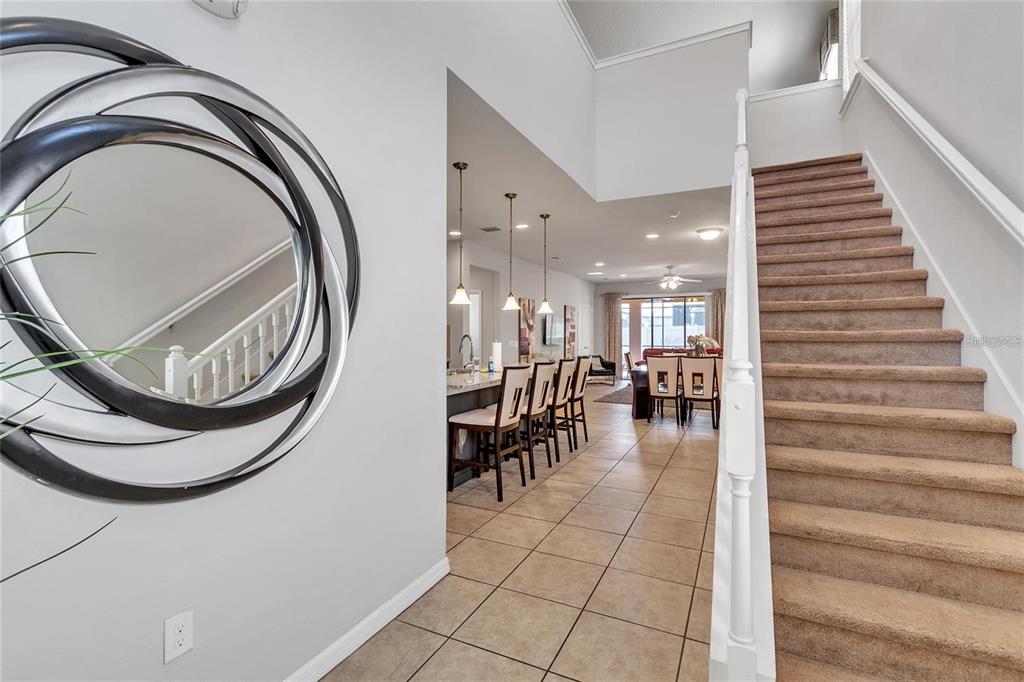 An entryway with a circular mirror, tiled floor, carpeted staircase, and a view into the kitchen — 8916 RHODES STREET, KISSIMMEE, FL