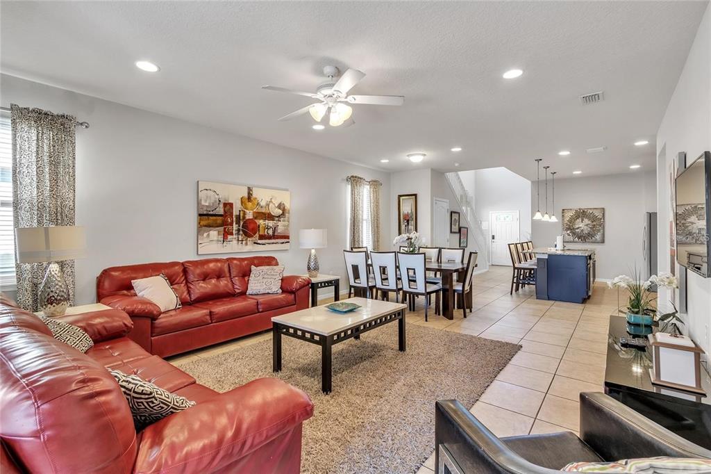 An open-concept living and dining area features red leather sofas, tile flooring, and a kitchen — 8916 RHODES STREET, KISSIMMEE, FL