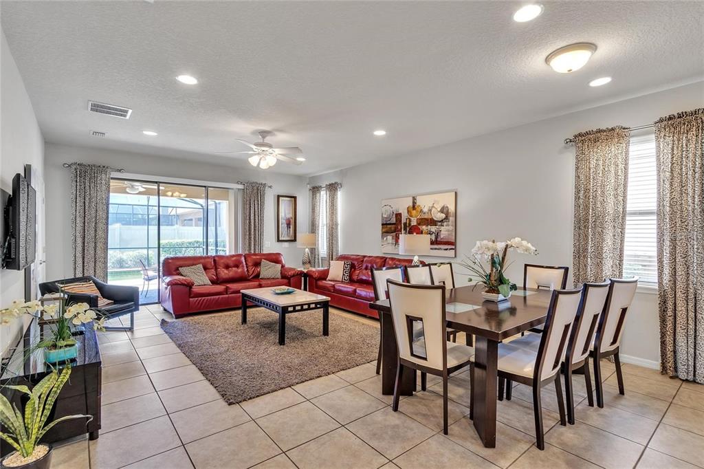 An open-concept living and dining area features red leather sofas, tile flooring, and large windows — 8916 RHODES STREET, KISSIMMEE, FL