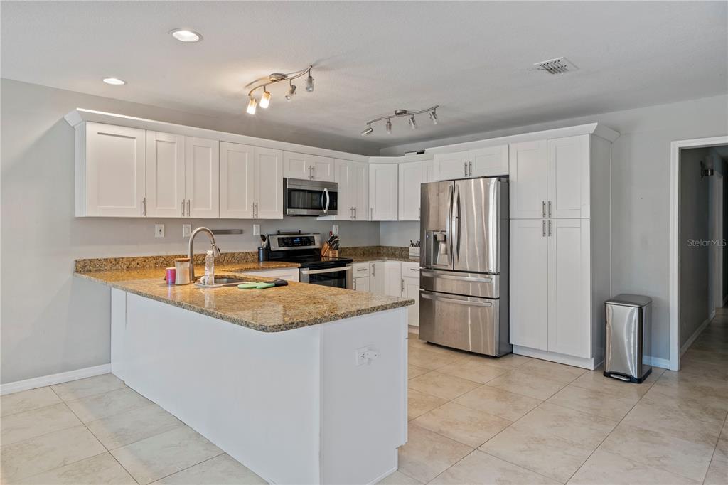 A kitchen features white cabinets, granite countertops, stainless steel appliances, and tile flooring — 37351 NEIGHBORS PATH, ZEPHYRHILLS, FL