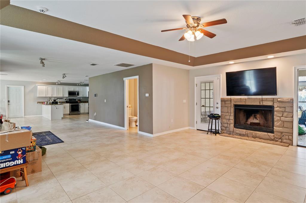This open-concept living area features tile flooring, a stone fireplace, and an adjacent kitchen — 37351 NEIGHBORS PATH, ZEPHYRHILLS, FL