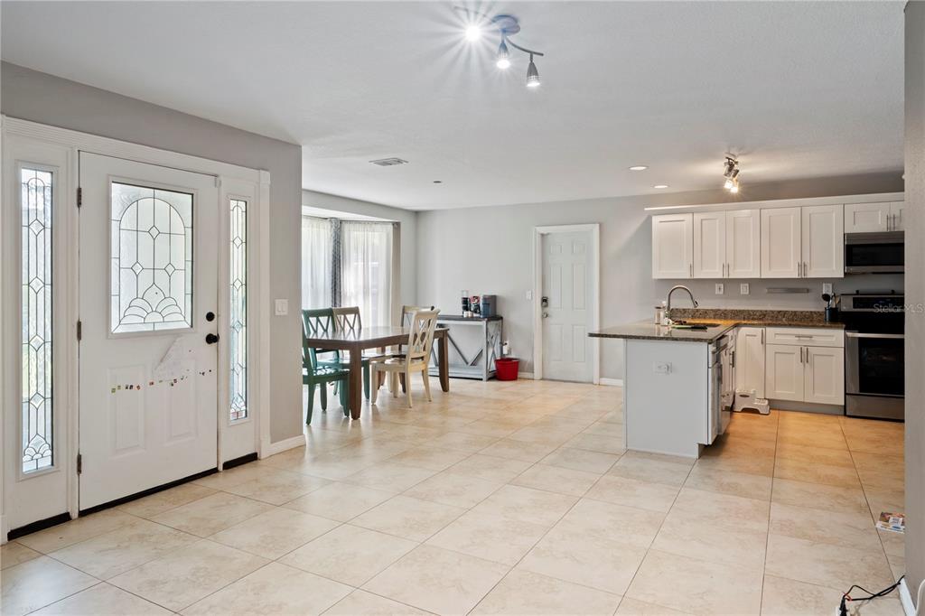 An open-concept kitchen and dining area features white cabinets, granite countertops, and light tile flooring — 37351 NEIGHBORS PATH, ZEPHYRHILLS, FL