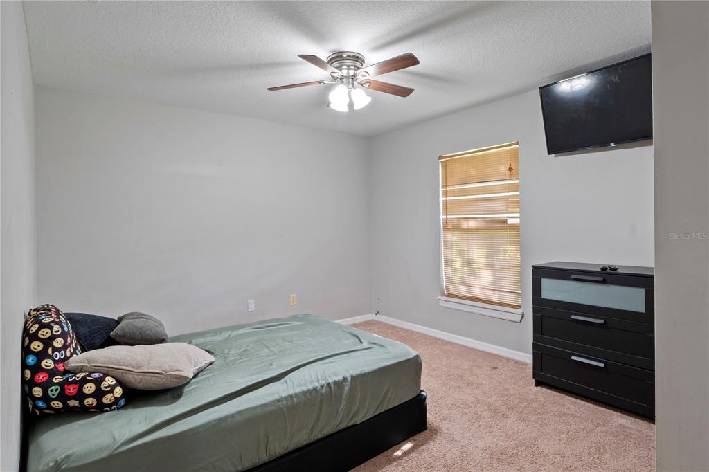 A bedroom features a bed with emoji-patterned pillows, a ceiling fan, and a black dresser — 37351 NEIGHBORS PATH, ZEPHYRHILLS, FL