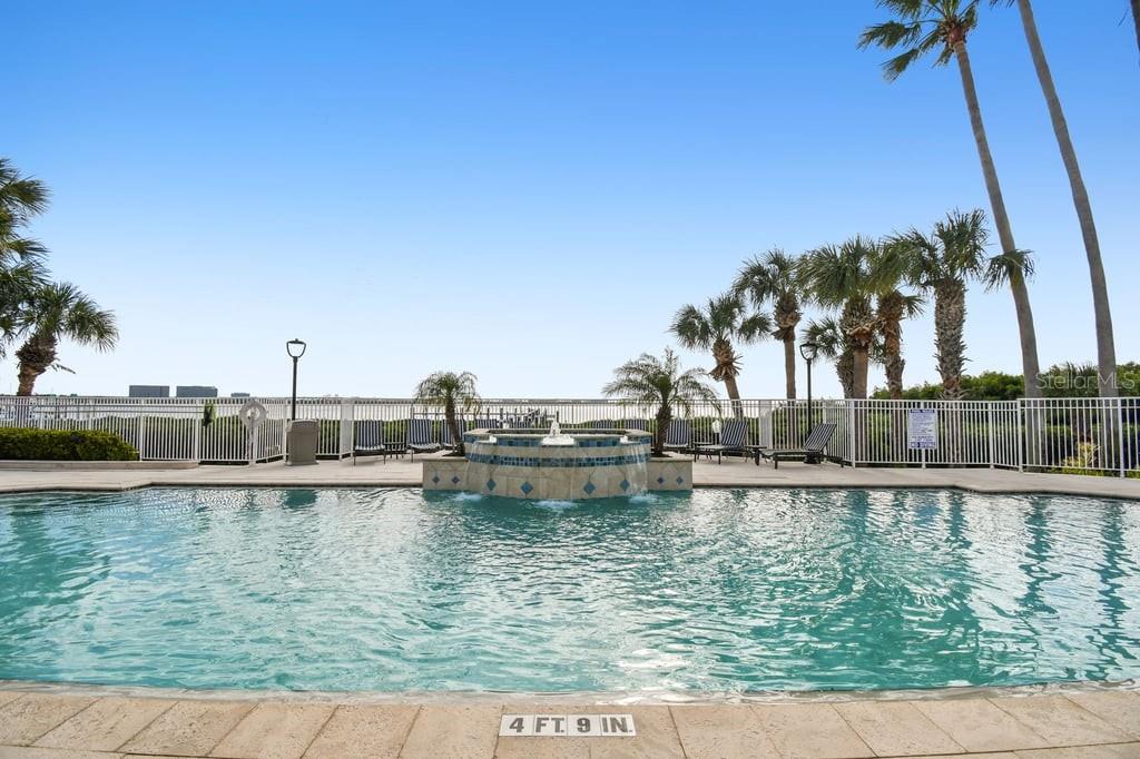 A swimming pool with a central fountain feature overlooks a body of water and palm trees — 4304 BAY CLUB CIRCLE UNIT 4304, TAMPA, FL
