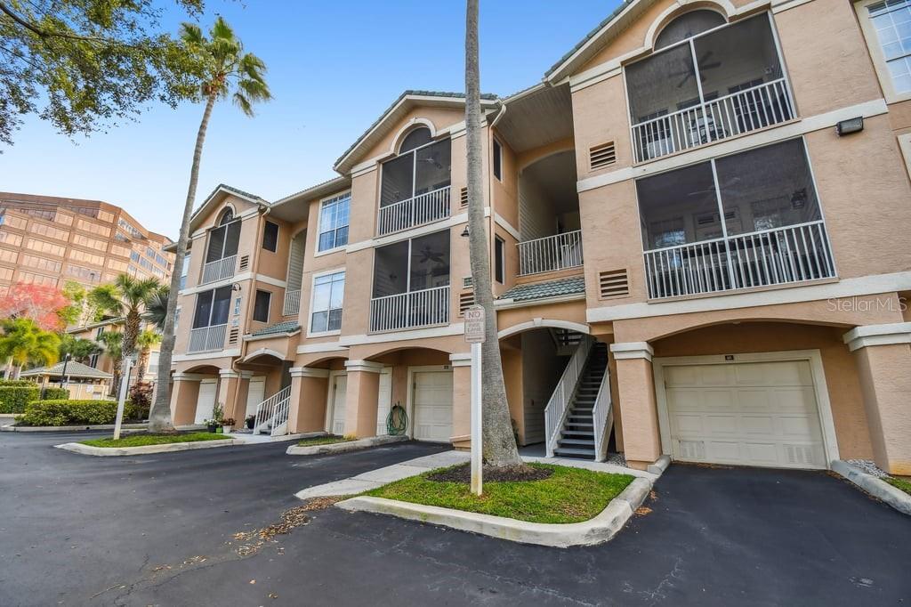 A three-story tan apartment building with screened balconies, attached garages, and an outdoor staircase — 4304 BAY CLUB CIRCLE UNIT 4304, TAMPA, FL
