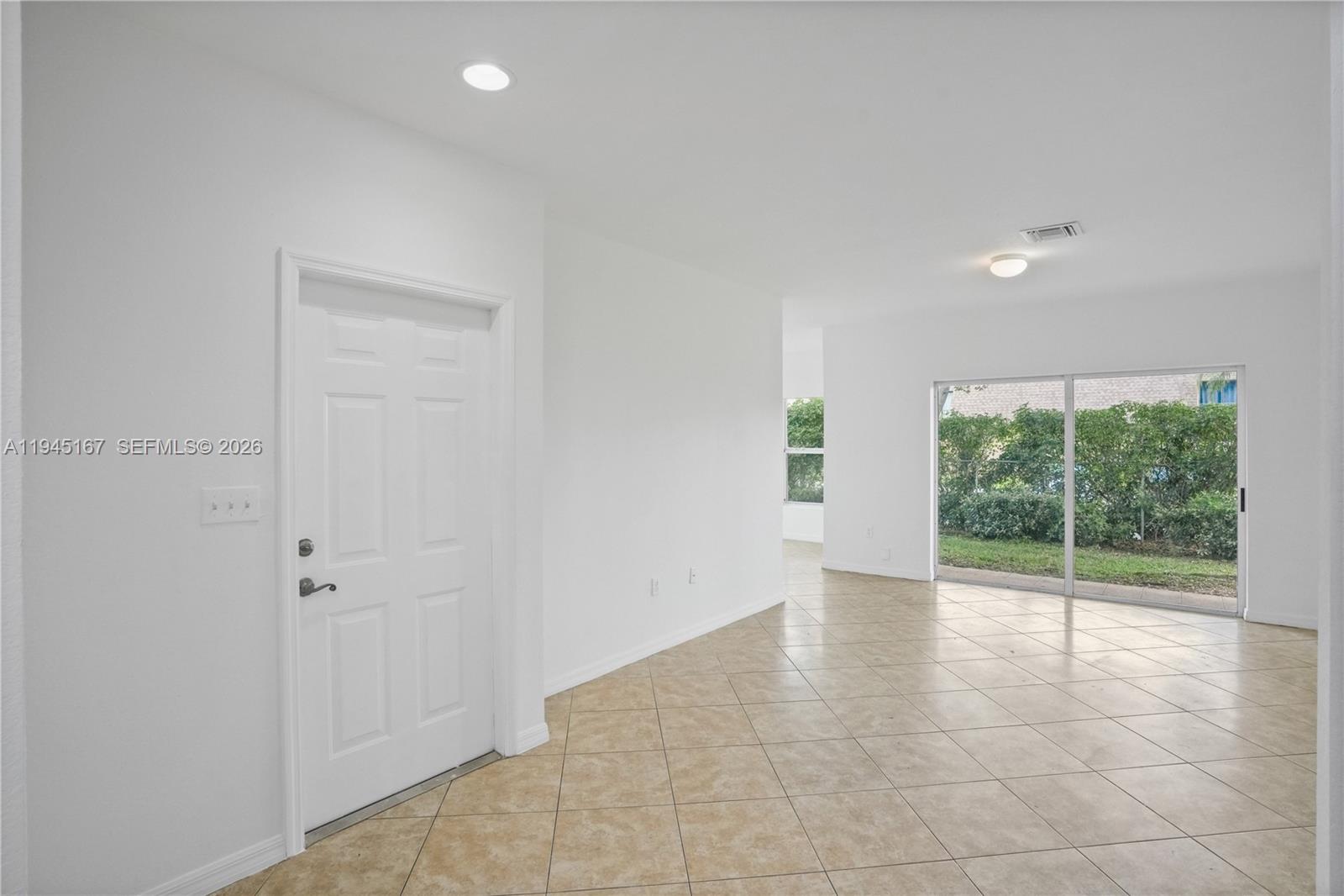 A bright, empty room features white walls, beige tile flooring, a white door, and sliding doors — 501 Talia Circle, Palm Springs FL 33461, PALM SPRINGS, FL