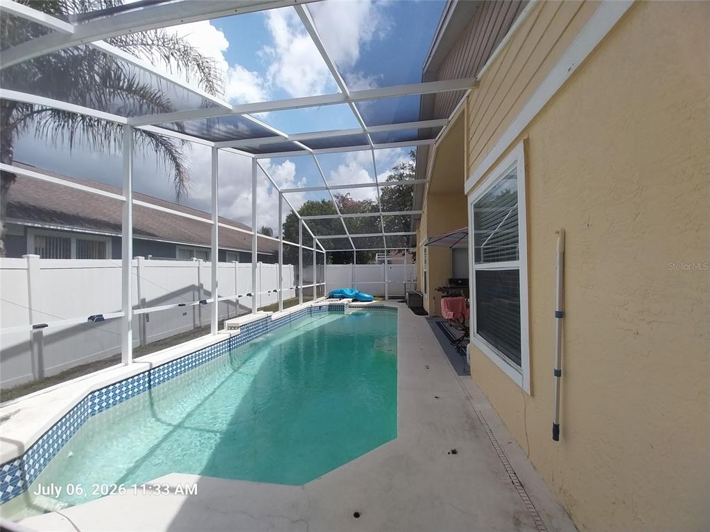 A screened-in swimming pool sits alongside a yellow house with a white fence — 17502 WOODTHRUSH PLACE, TAMPA, FL