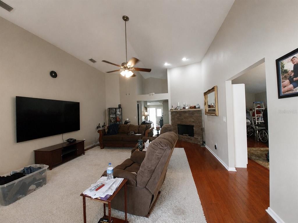 A living room features a large television, a stone fireplace, and vaulted ceilings — 17502 WOODTHRUSH PLACE, TAMPA, FL