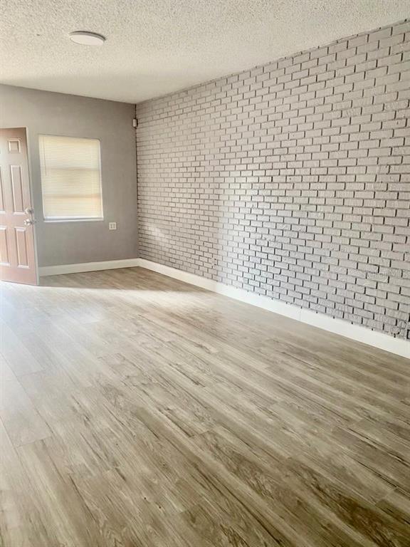 An empty room features light wood-look flooring, a white painted brick wall, and a window — 3356 AVENUE Q NW, WINTER HAVEN, FL