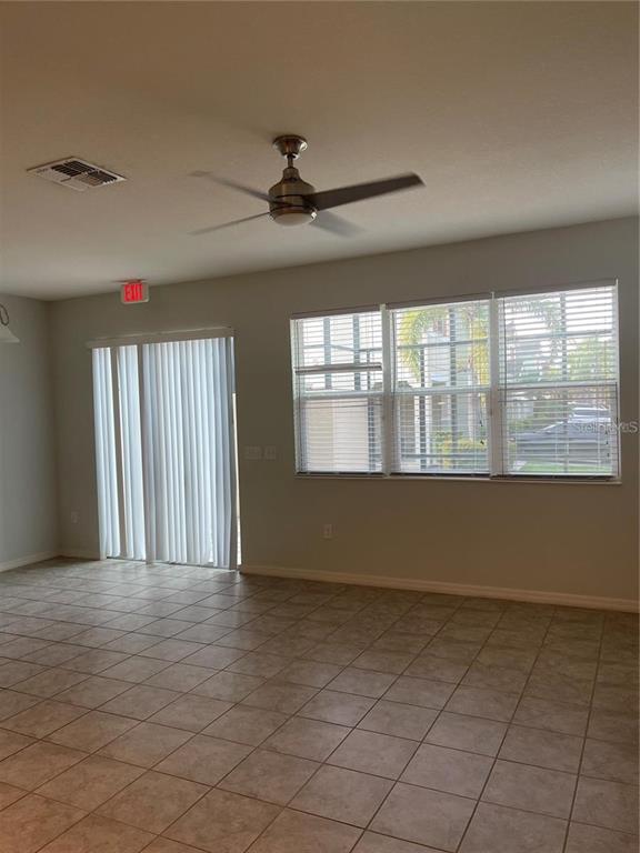 An empty room features tile flooring, a ceiling fan, sliding glass doors, and large windows — 3129 TOCOA CIRCLE, KISSIMMEE, FL