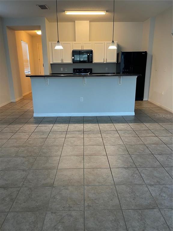 A kitchen features white cabinets, black appliances, a breakfast bar, and tiled flooring — 3129 TOCOA CIRCLE, KISSIMMEE, FL