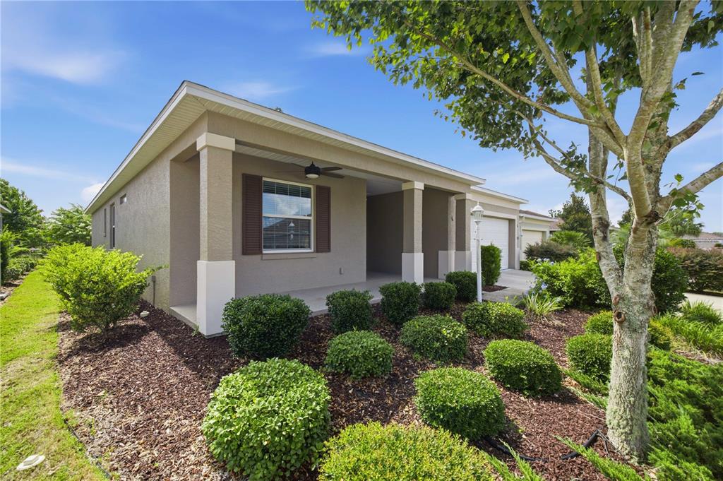 A tan single-story house features a covered front porch, brown shutters, and landscaped mulch beds — 8525 SW 79TH AVENUE, OCALA, FL
