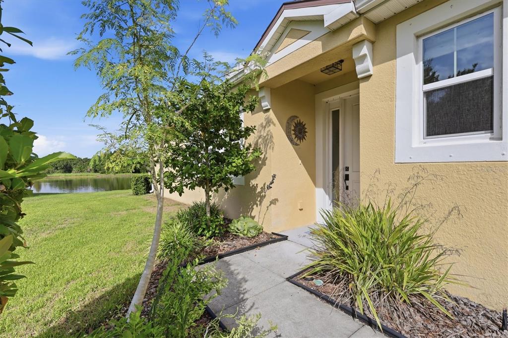 A tan house exterior features a front walkway, landscaping, and a view of a pond — 11474 ROLLING GREEN DRIVE, BRADENTON, FL