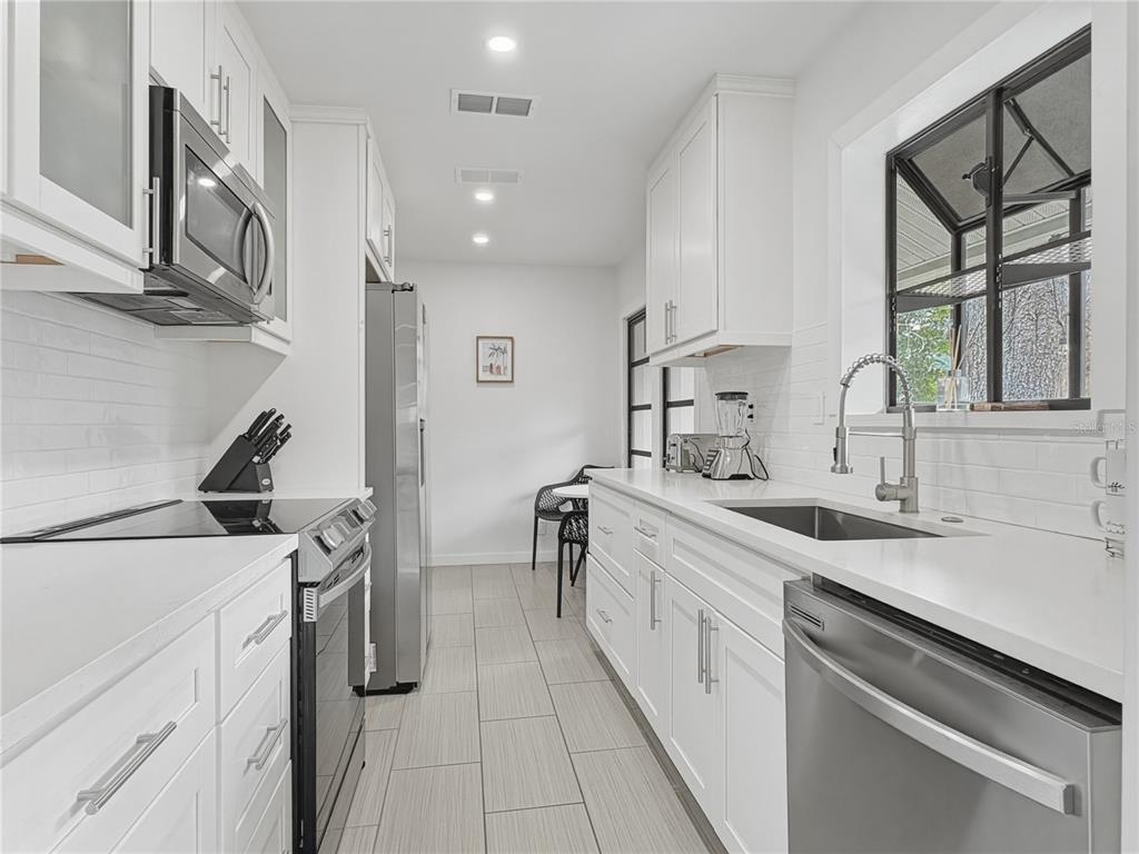 A galley kitchen features white cabinets, stainless steel appliances, quartz countertops, and light tile flooring — 2026 GROVE STREET, SARASOTA, FL