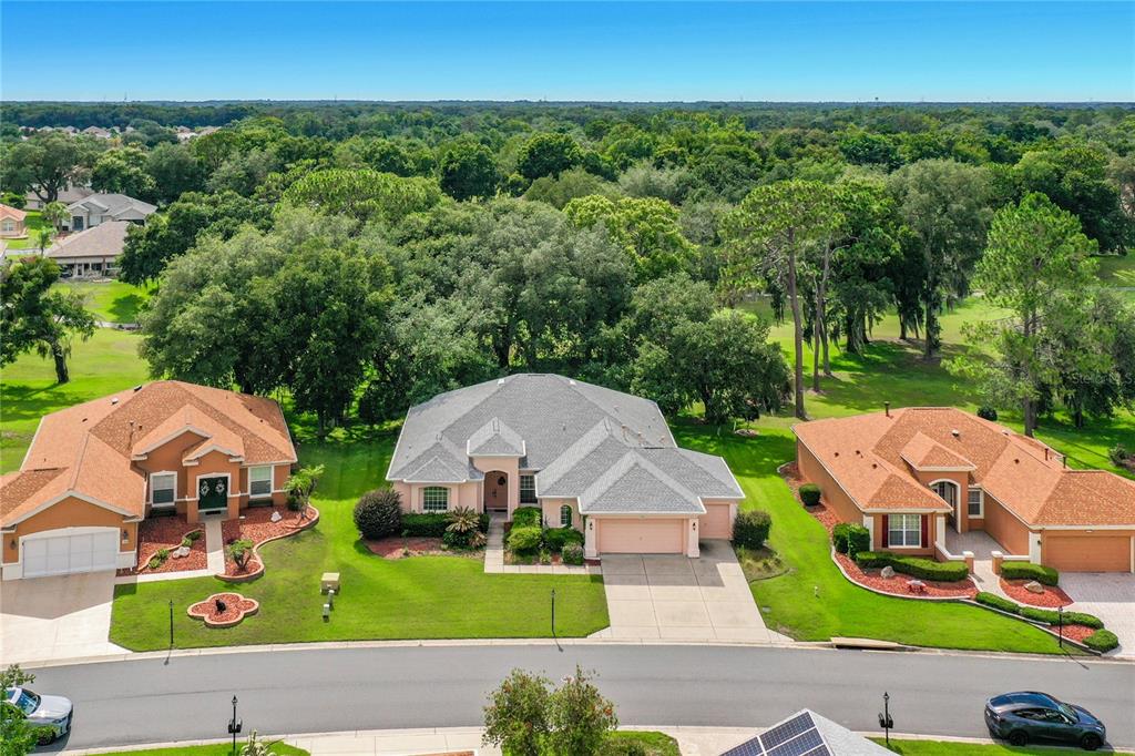 An aerial view shows three suburban houses with manicured lawns and a wooded background — 12992 SE 91ST COURT, SUMMERFIELD, FL