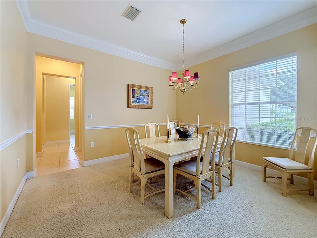 A dining room features a light-colored table, six chairs, a chandelier, and beige carpeting — 12992 SE 91ST COURT, SUMMERFIELD, FL