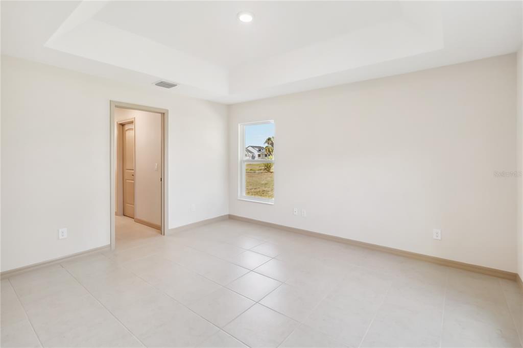 An empty room with light-colored tile flooring, a tray ceiling, and a single window — 4255 TUCKER AVENUE, ST CLOUD, FL
