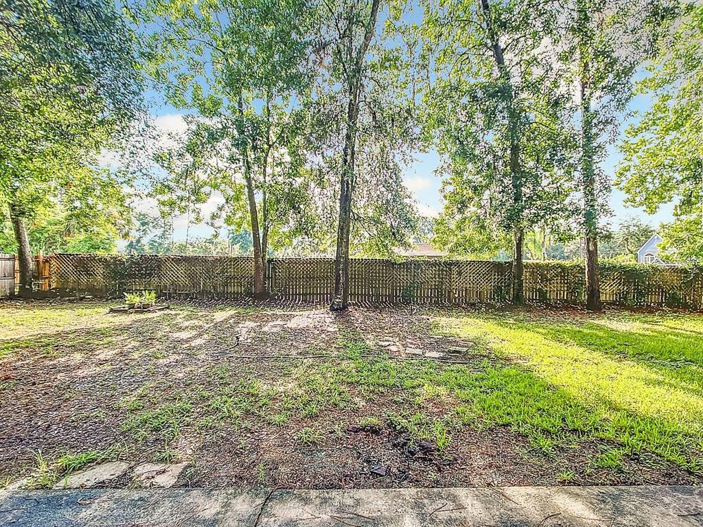 A grassy backyard features a lattice fence and several tall trees under a blue sky — 3729 SW 15 STREET, GAINESVILLE, FL