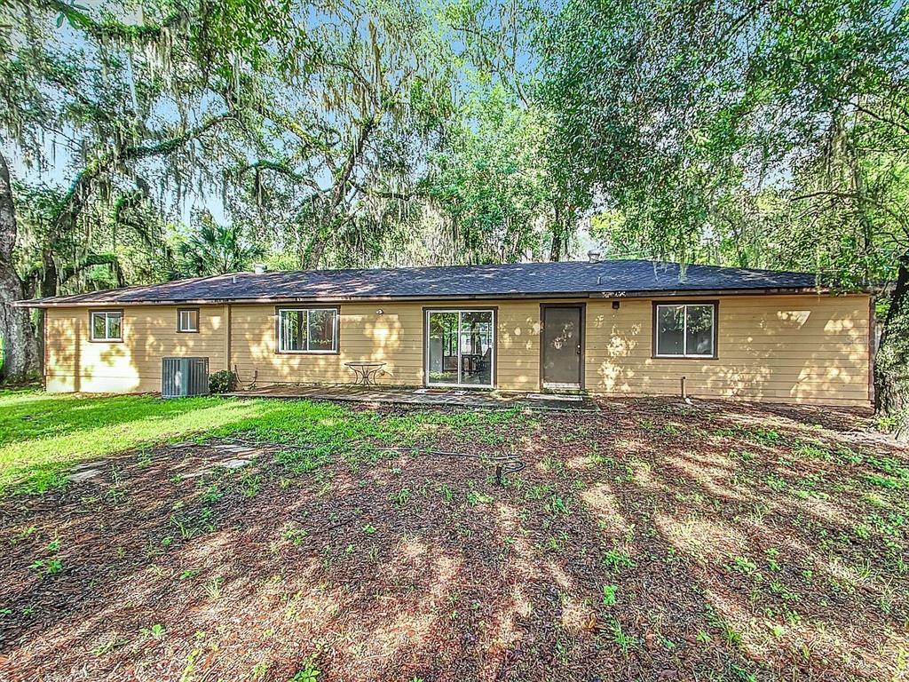 The rear exterior of a single-story house features tan siding, a dark roof, and trees — 3729 SW 15 STREET, GAINESVILLE, FL