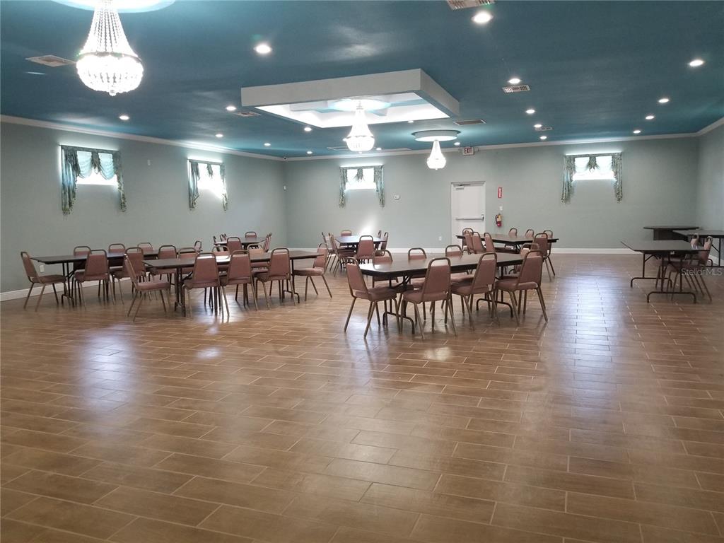 A large event hall features a blue ceiling, tile flooring, and multiple tables with chairs — 2240 MARCELLA WAY, LEESBURG, FL