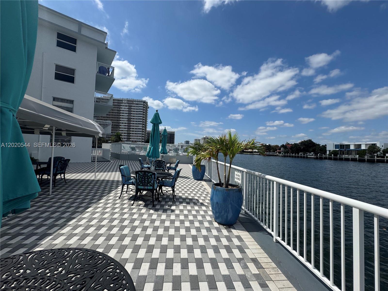 A patio with checkered pavers, outdoor furniture, and potted plants overlooks a waterfront canal — 1913 S Ocean Dr # 427, Hallandale Beach FL 33009, HALLANDALE BEACH, FL