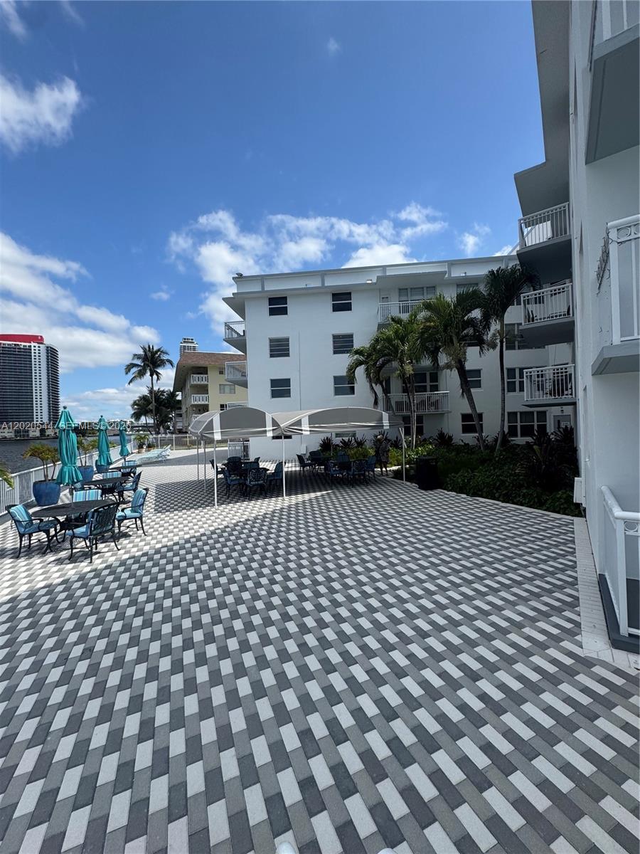 A paved patio area features outdoor tables, chairs, and a canopy beside a white building — 1913 S Ocean Dr # 427, Hallandale Beach FL 33009, HALLANDALE BEACH, FL