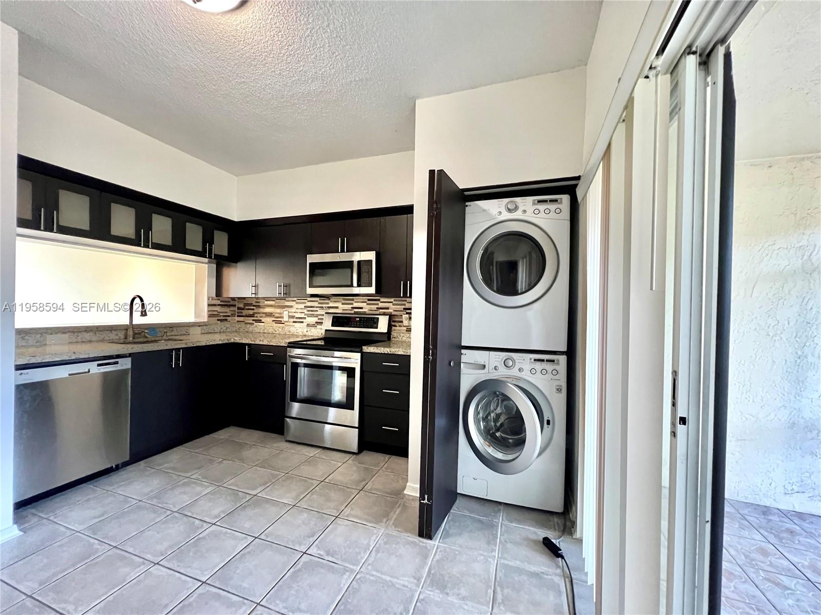 A kitchen features dark cabinets, stainless steel appliances, tiled floors, and a stacked laundry unit — 271 Duval Ct, Weston FL 33326, WESTON, FL