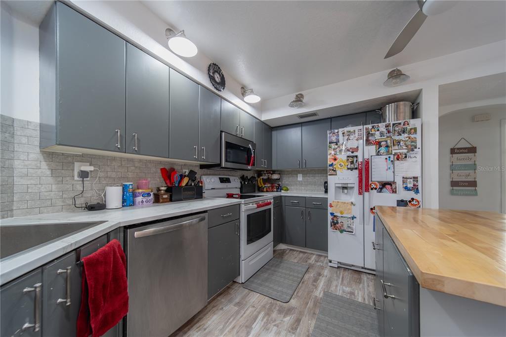 A kitchen features gray cabinets, stainless steel appliances, a white countertop, and a wood island — 1157 BEAUMONT AVENUE, PORT CHARLOTTE, FL