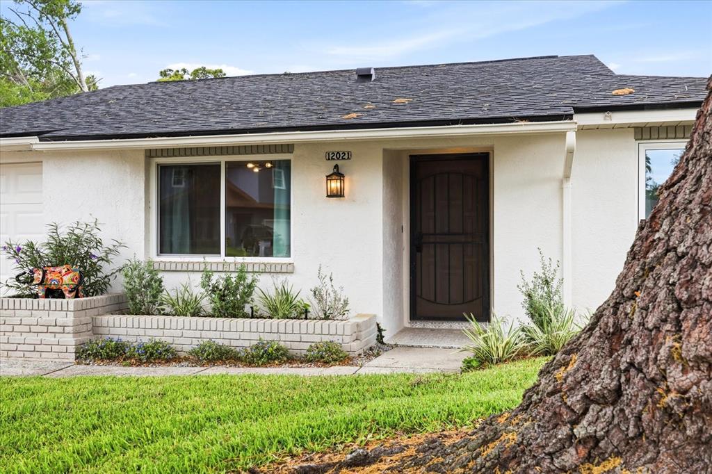 A single-story house with white stucco walls, a dark roof, and a brick planter box — 12021 107TH COURT, LARGO, FL