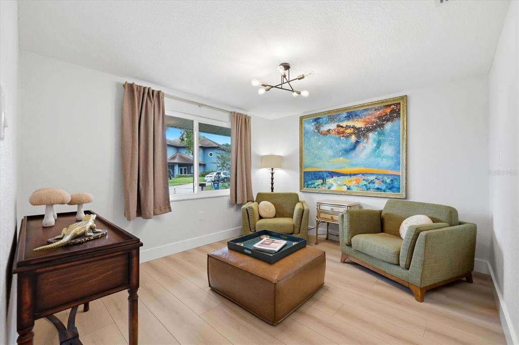 A living room features two green armchairs, a leather ottoman, and a large abstract painting — 12021 107TH COURT, LARGO, FL