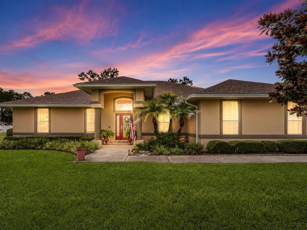 A single-story tan house with a red front door and a lush green lawn at sunset — 170 OLD NICHOLS CIRCLE, AUBURNDALE, FL
