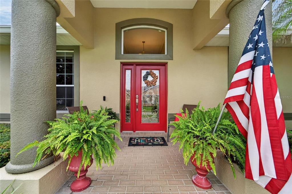 A red front door with a wreath and an American flag stands on a brick porch — 170 OLD NICHOLS CIRCLE, AUBURNDALE, FL