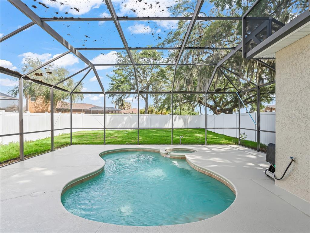 A screened-in pool and spa area with a concrete deck and a fenced backyard — 4942 NE 123RD LANE, OXFORD, FL
