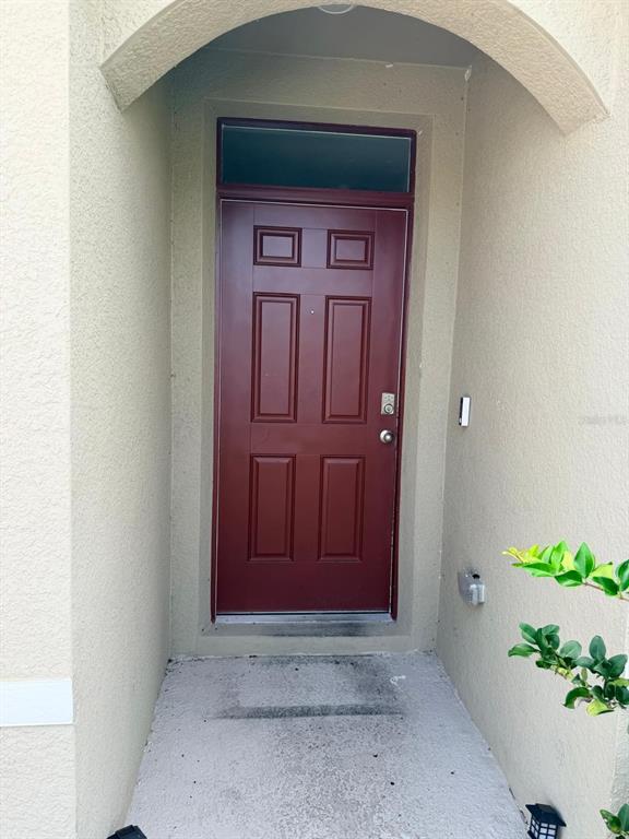 A red six-panel front door is recessed within a beige stucco entryway — 1229 RED HILL ROAD, DAVENPORT, FL