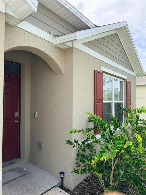 A tan stucco house exterior features a red front door and a window with red shutters — 1229 RED HILL ROAD, DAVENPORT, FL