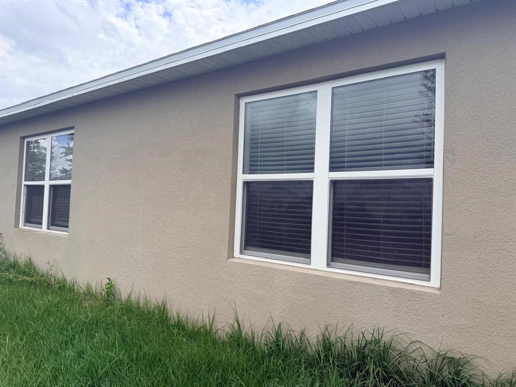 The exterior view shows a tan stucco wall with two white-framed windows and tall grass — 1229 RED HILL ROAD, DAVENPORT, FL