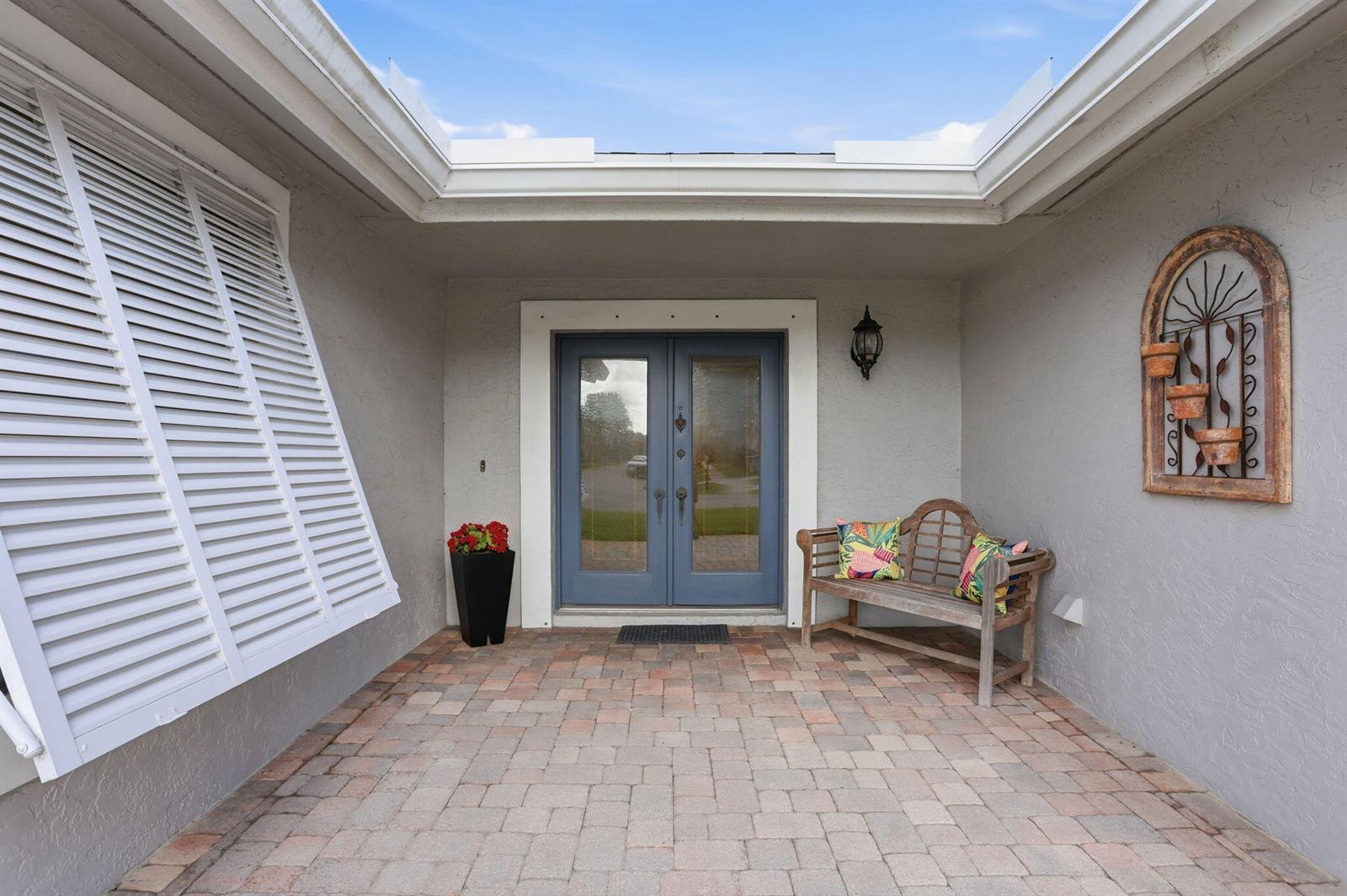 A covered entryway features a brick paver floor, double blue doors, and a wooden bench — 4281 Sugar Pine Drive, Boca Raton FL 33487, BOCA RATON, FL