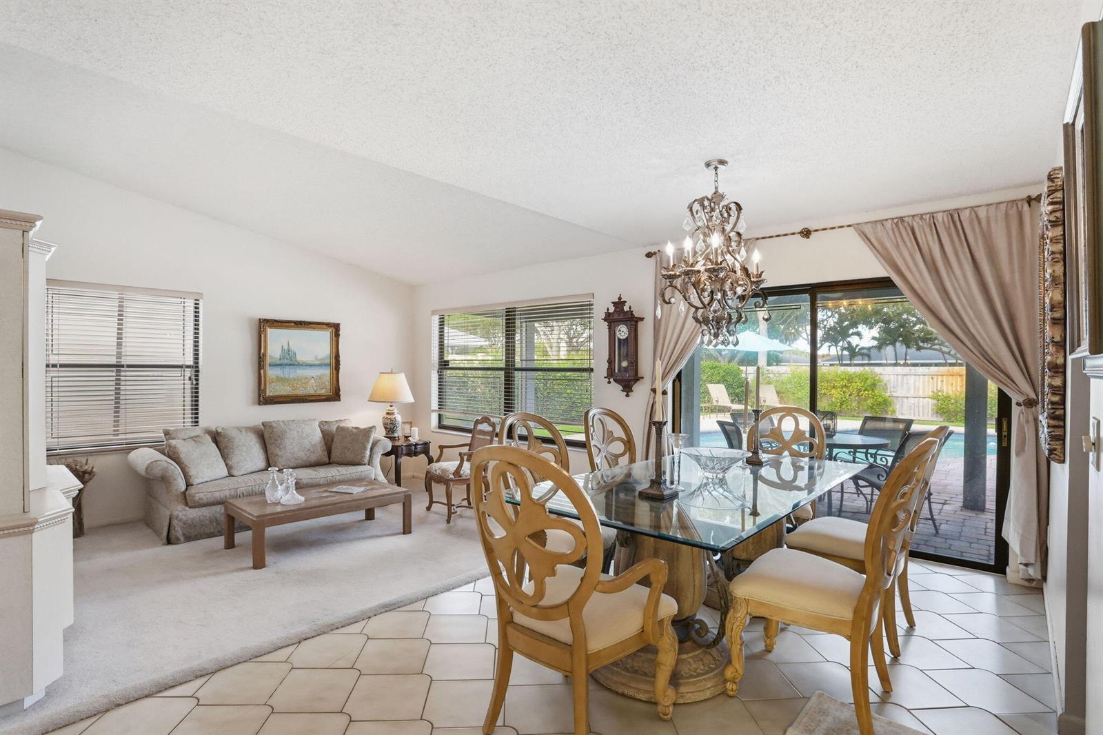 A dining area with a glass table and chandelier sits next to a carpeted living room — 4281 Sugar Pine Drive, Boca Raton FL 33487, BOCA RATON, FL