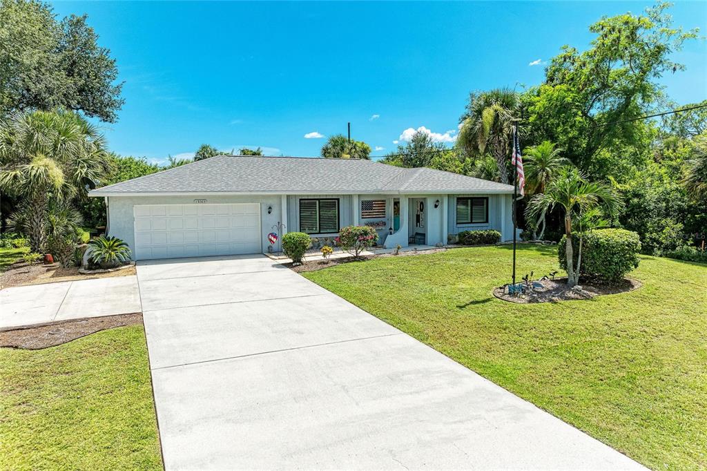 A single-story house with a white garage, gray roof, and a front lawn with trees — 18565 EDGEWATER DRIVE, PORT CHARLOTTE, FL