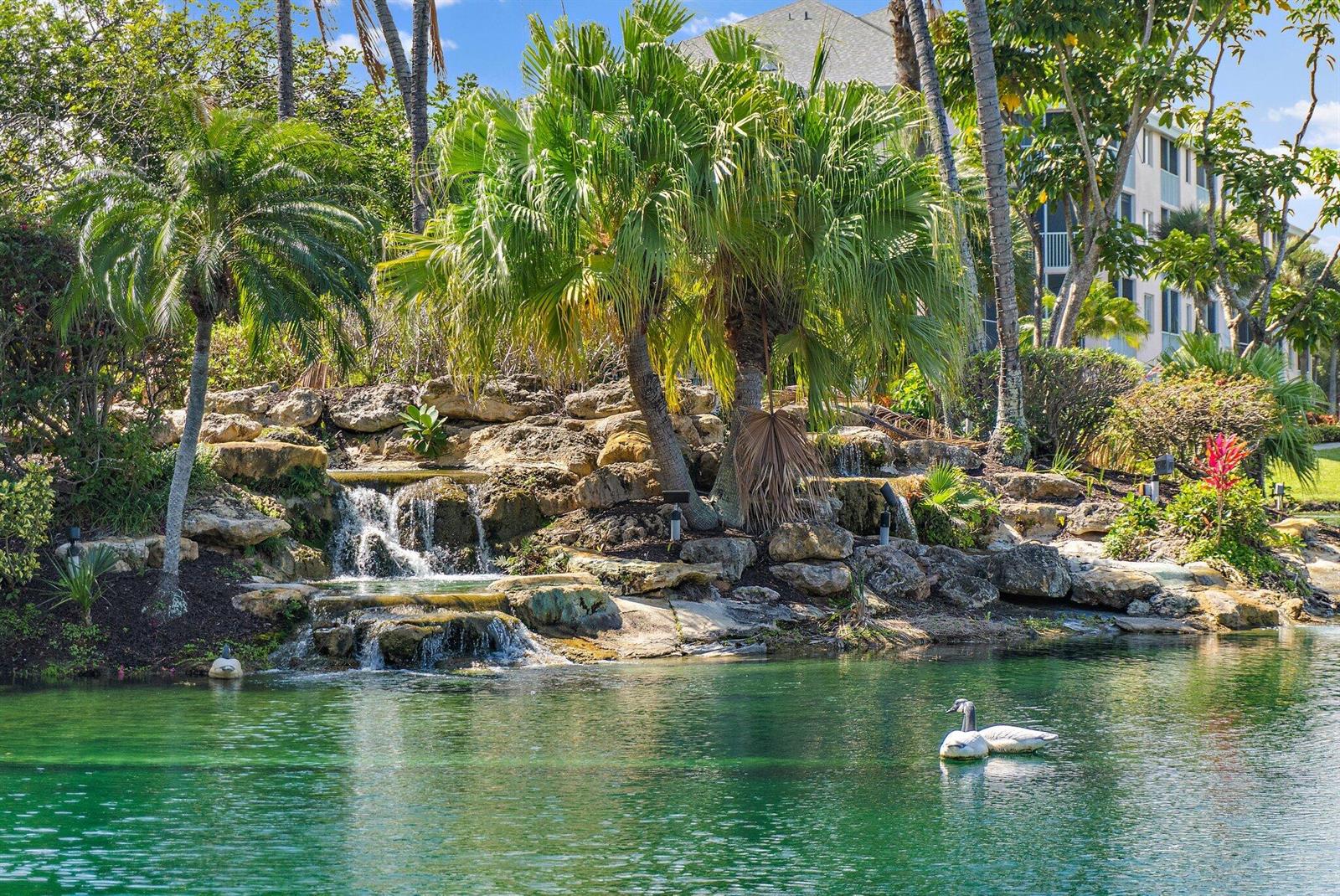 An aerial view shows a pond with a landscaped island featuring waterfalls and palm trees — 353 S Us-1 # C106, Jupiter FL 33477, JUPITER, FL