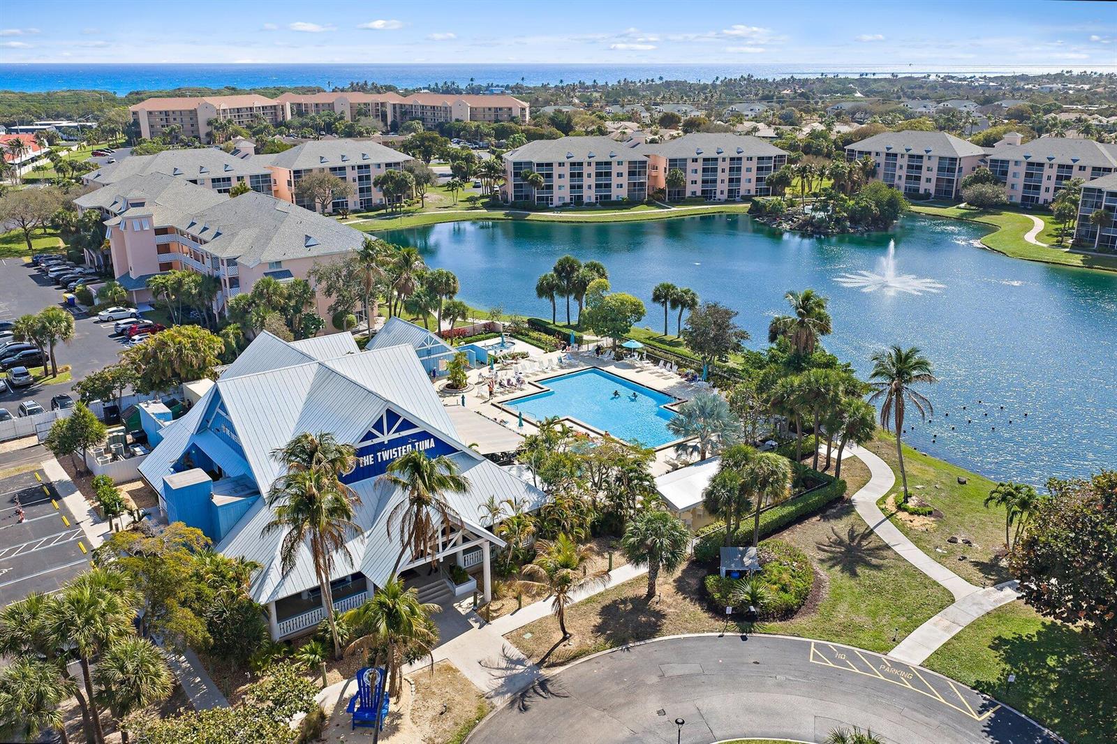 An aerial view shows multi-story apartment buildings surrounding a lake with a central fountain — 353 S Us-1 # C106, Jupiter FL 33477, JUPITER, FL