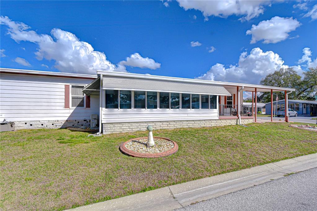 A white mobile home with a large enclosed porch and a small stone birdbath outside — 35909 BUENO DRIVE, ZEPHYRHILLS, FL