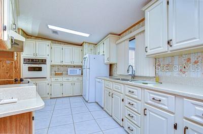 A kitchen features white cabinetry, light-colored countertops, tiled flooring, and a built-in wall oven — 35909 BUENO DRIVE, ZEPHYRHILLS, FL