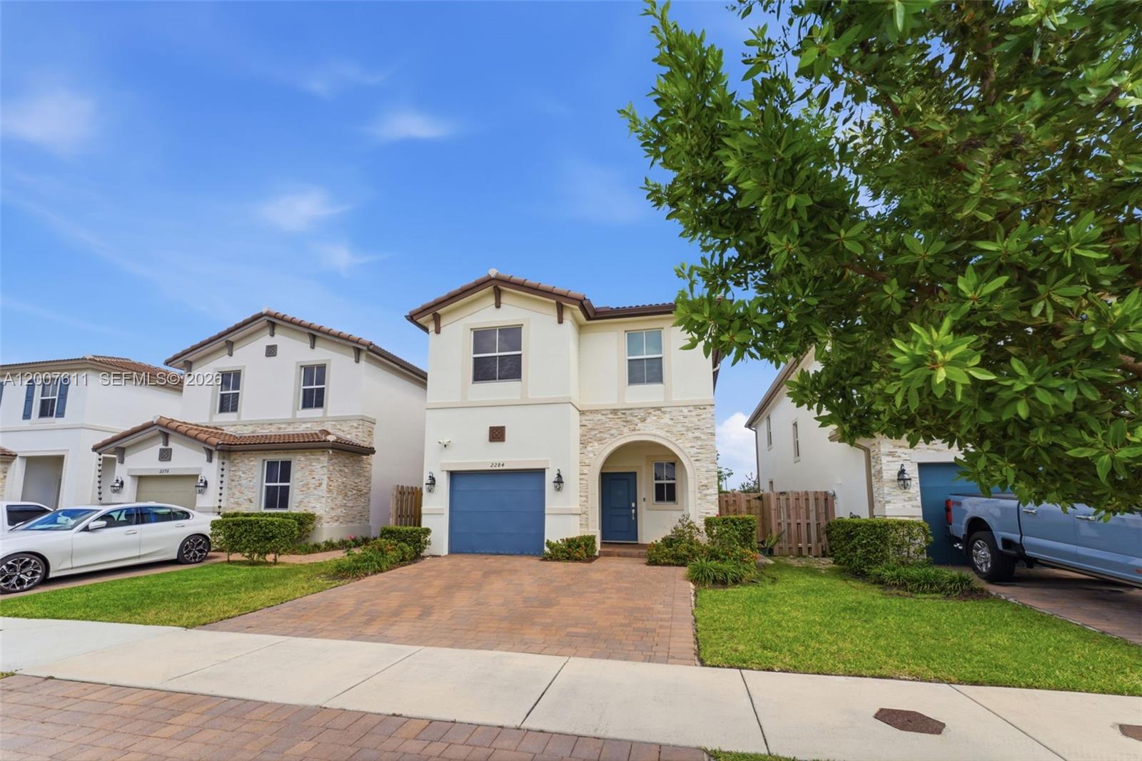 A two-story suburban house with a blue garage door, stone accents, and a paved driveway — 2284 NW 130th St # 0, Miami FL 33167, MIAMI, FL