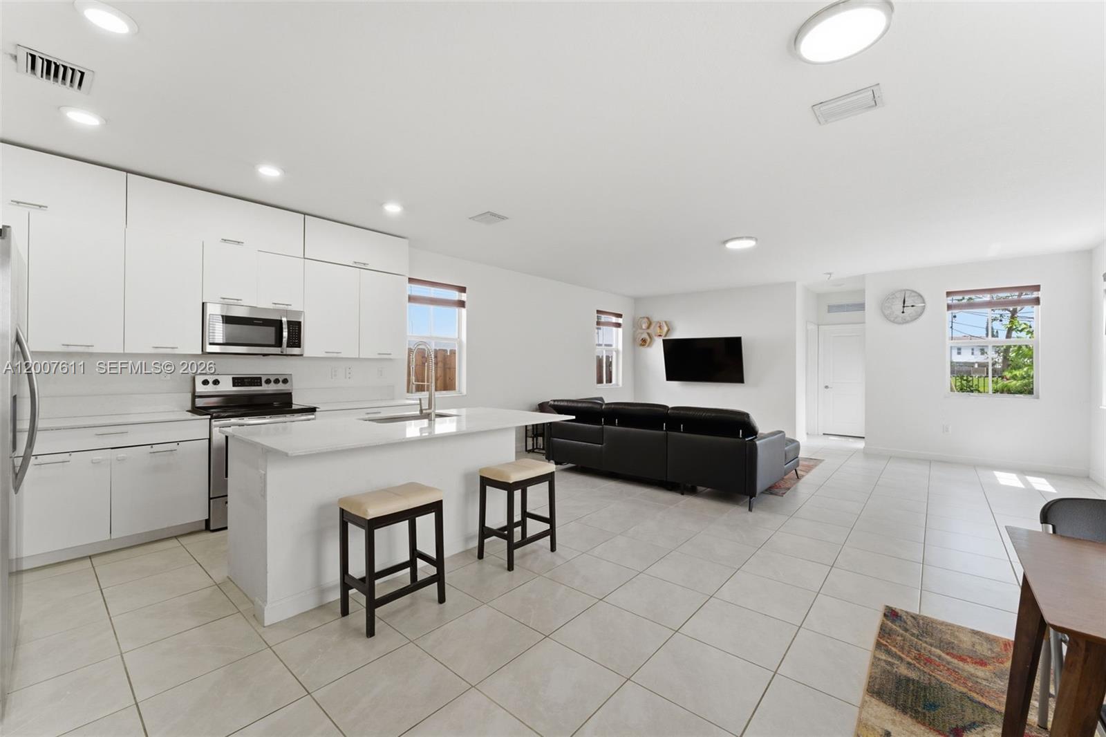 An open-concept kitchen and living area features white cabinetry, a kitchen island, and tile flooring — 2284 NW 130th St # 0, Miami FL 33167, MIAMI, FL