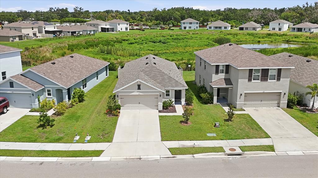 An aerial view shows three suburban houses with driveways and lawns facing a grassy retention pond — 5051 GRANITE DUST PLACE, PALMETTO, FL