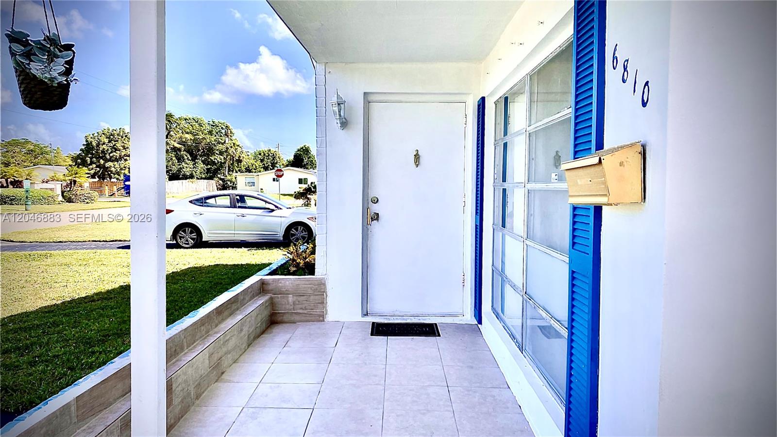 A covered front porch features tiled flooring, a white door, and blue window shutters — 6810 NW 28th St, Sunrise FL 33313, SUNRISE, FL